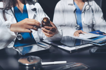 Two doctors and a female nurse meet at a table in the hospital, collaborating on medical tasks using laptops and computersの写真素材