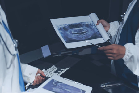 Two doctors and a female nurse meet at a table in the hospital, collaborating on medical tasks using laptops and computersの写真素材