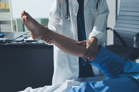 Doctor examining and supporting injured ankle of female patient in hospital room, providing medical assistance and treatment for sprain or fractureの写真素材