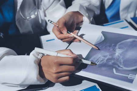 Two doctors and a female nurse meet at a table in the hospital, collaborating on medical tasks using laptops and computersの写真素材