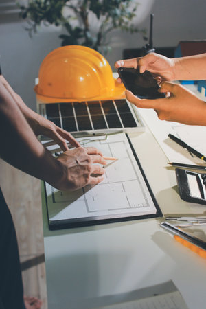 Closeup of team of engineers meeting analyze machinery blueprints consult project on table in...