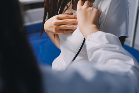 Doctor examining patient with stethoscope in hospital bed. Medical care and healthcare concept in a clinical setting.の写真素材