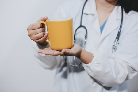 Portrait of Asian doctor woman standing holding coffee cup in white studio backgroundの写真素材