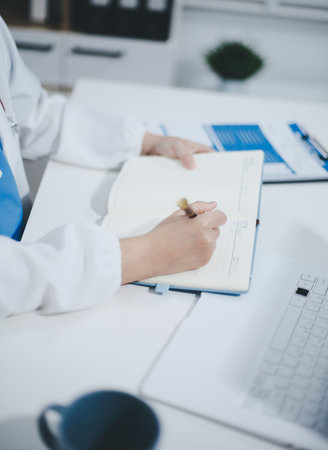 Middle aged female doctor working on laptop in doctor's roomの写真素材