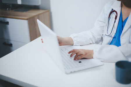Middle aged female doctor working on laptop in doctor's roomの写真素材