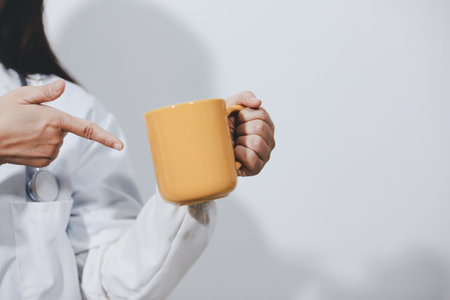 Portrait of Asian doctor woman standing holding coffee cup in white studio backgroundの写真素材