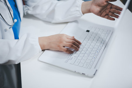 Middle aged female doctor working on laptop in doctor's roomの写真素材