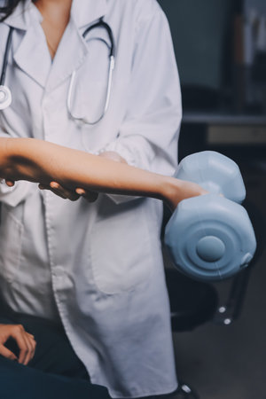 old woman training with physiotherapist using dumbbells at home therapist assisting senior woman with exercises in nursing home elderly patient using dumbbells with outstretched arms no logos no branの写真素材