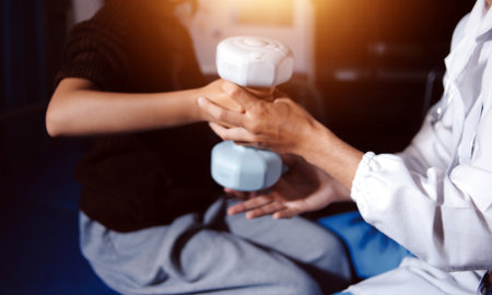 Old woman training with physiotherapist using dumbbells at home. Therapist assisting senior woman with exercises in nursing home. Elderly patient using dumbbells with outstretched arms.の写真素材