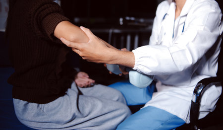 Old woman training with physiotherapist using dumbbells at home. Therapist assisting senior woman with exercises in nursing home. Elderly patient using dumbbells with outstretched arms.の写真素材