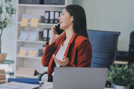 Serious charming woman using smartphone while working with laptopの写真素材