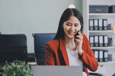 Serious charming woman using smartphone while working with laptopの写真素材