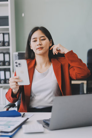 Serious charming woman using smartphone while working with laptopの写真素材