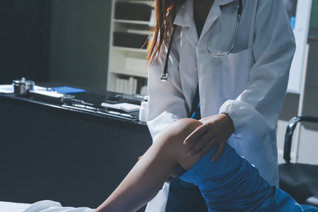 Doctor examining and supporting injured ankle of female patient in hospital room, providing medical assistance and treatment for sprain or fractureの写真素材