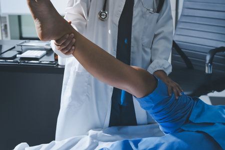Doctor examining and supporting injured ankle of female patient in hospital room, providing medical assistance and treatment for sprain or fractureの写真素材