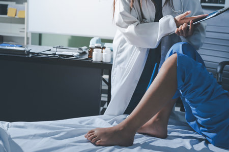 Doctor examining and supporting injured ankle of female patient in hospital room, providing medical assistance and treatment for sprain or fractureの写真素材