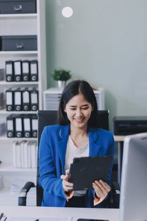 A smiling woman in a lab coat uses a tablet in a bright, modern environment.の写真素材