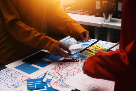 Team of uxui designers pointing at computer screen, discussing new mobile app design in the officeの写真素材