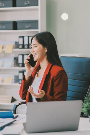 Serious charming woman using smartphone while working with laptop