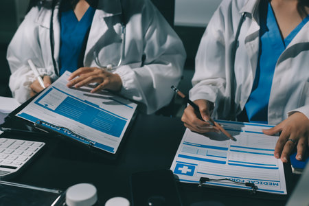Two doctors and a female nurse meet at a table in the hospital, collaborating on medical tasks using...