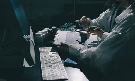 Two doctors and a female nurse meet at a table in the hospital, collaborating on medical tasks using...