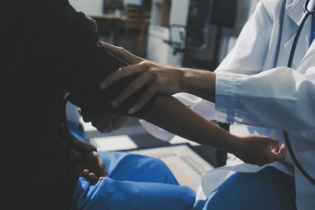 Doctor in hospital using manual blood pressure monitor to measure woman patient blood pressure and...