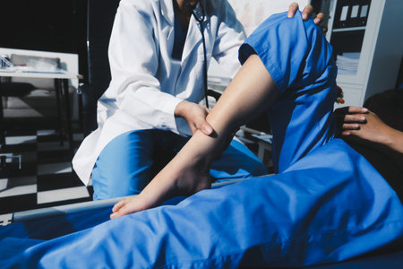 Asian male doctor examining foot of female patient sitting on bed in hospital room. Performing medical checkup. Diagnosing injury. Providing healthcare. Podiatry. Physical therapy. And rehabilitationの写真素材
