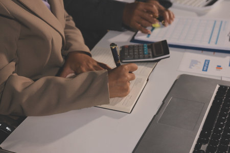 business documents on office table with tablet, smart phone and laptop and two colleagues discussing...