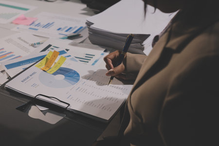 business documents on office table with tablet, smart phone and laptop and two colleagues discussing dataの写真素材