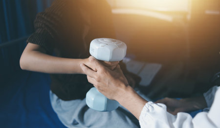 Old woman training with physiotherapist using dumbbells at home. Therapist assisting senior woman with exercises in nursing home. Elderly patient using dumbbells with outstretched arms.の写真素材