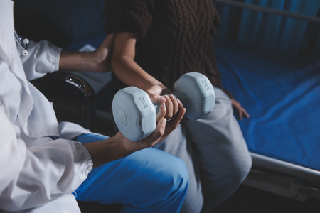 Old woman training with physiotherapist using dumbbells at home. Therapist assisting senior woman with exercises in nursing home. Elderly patient using dumbbells with outstretched arms.の写真素材