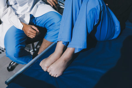 Asian male doctor examining foot of female patient sitting on bed in hospital room. Performing...