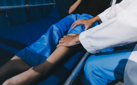 Asian male doctor examining foot of female patient sitting on bed in hospital room. Performing medical checkup. Diagnosing injury. Providing healthcare. Podiatry. Physical therapy. And rehabilitationの写真素材