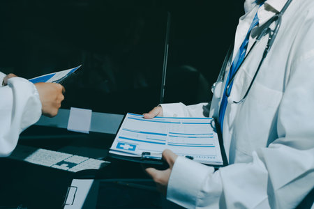 Two doctors and a female nurse meet at a table in the hospital, collaborating on medical tasks using...