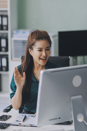 Asian businesswoman works in a modern office, confidently analyzing data on her laptop, embodying...