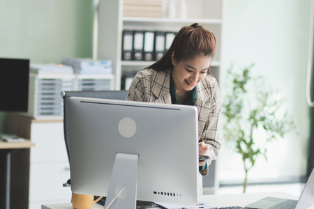 Determined asian businesswoman works late in a modern office, confidently analyzing data on her...