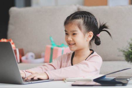 A cheerful Asian mother helps her young daughter do homework and color a book at home, while the...