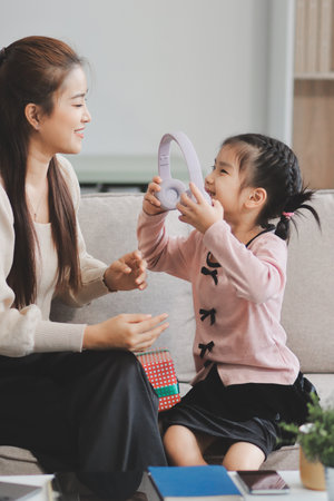 A cheerful Asian mother helps her young daughter do homework and color a book at home, while the...