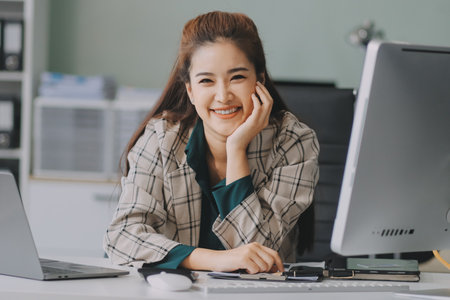 Cheerful business lady working on laptop in office, Asian happy beautiful businesswoman in formal suit work in workplace. Attractive female employee office worker smile.の写真素材