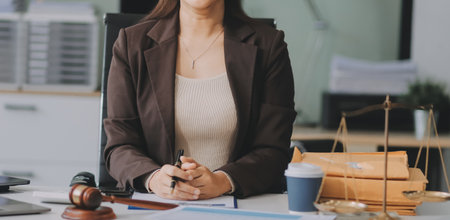 Confident Lawyer Working at Desk: A young Asian female lawyer confidently works on her laptop,...