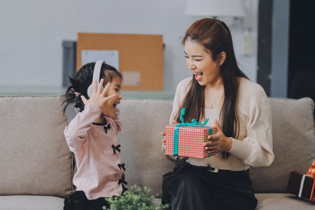 A cheerful Asian mother helps her young daughter do homework and color a book at home. A cozy, bright, and modern family lifestyle.の写真素材