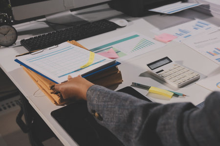 business documents on office table with tablet, smart phone and laptop and two colleagues discussing dataの写真素材