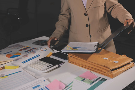 business documents on office table with tablet, smart phone and laptop and two colleagues discussing dataの写真素材