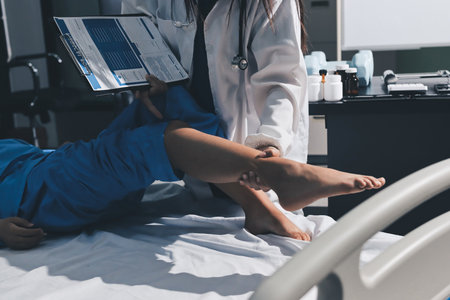 Doctor examining and supporting injured ankle of female patient in hospital room, providing medical assistance and treatment for sprain or fractureの写真素材