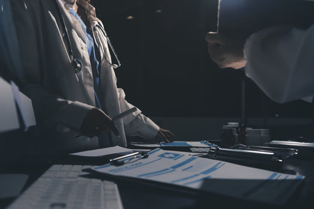 Two doctors and a female nurse meet at a table in the hospital, collaborating on medical tasks using...