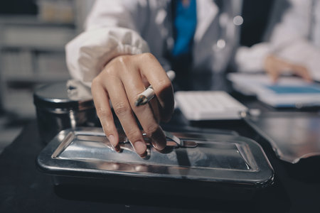 Two doctors and a female nurse meet at a table in the hospital, collaborating on medical tasks using laptops and computersの写真素材
