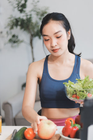 Fit young Asian women in activewear sitting on yoga mat and eating fresh vegetable salad after workout, representing clean eating, fitness lifestyle, wellness routine and health balance.の写真素材
