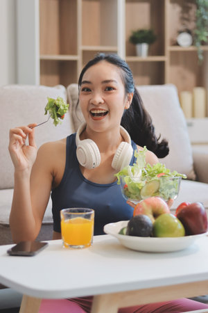 Fit young Asian women in activewear sitting on yoga mat and eating fresh vegetable salad after workout, representing clean eating, fitness lifestyle, wellness routine and health balance.の写真素材