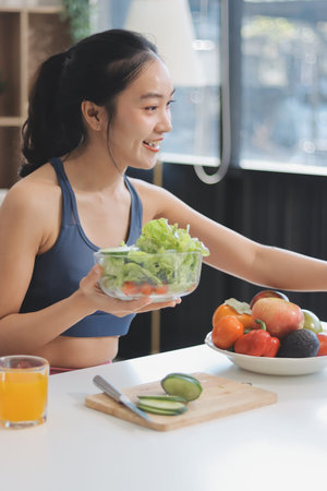 Fit young Asian women in activewear sitting on yoga mat and eating fresh vegetable salad after workout, representing clean eating, fitness lifestyle, wellness routine and health balance.の写真素材