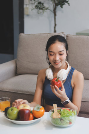 Fit young Asian woman in activewear sitting on yoga mat and eating fresh vegetable salad after workout, representing clean eating, fitness lifestyle, wellness routine and health balance.の写真素材